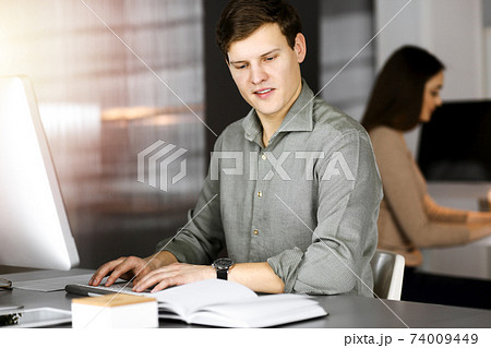 Young businessman working on his computer sitting at the desk in office. Headshot portrait of a man Young businessman working on his computer sitting at the desk in office. Headshot portrait of a man 74009449