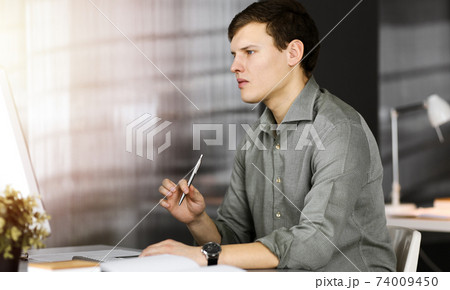 Young businessman working on his computer sitting at the desk in office. Headshot portrait of a man 74009450