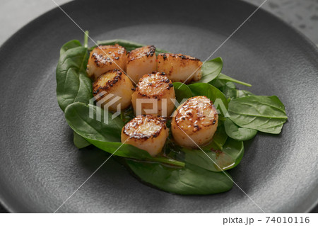 Seared scallops on pile of spinach on black plate closeup Seared scallops on pile of spinach on black plate closeup 74010116