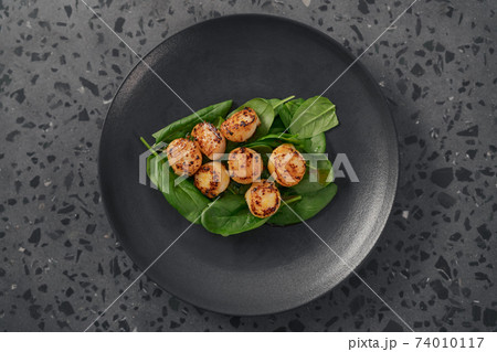 Seared scallops on pile of spinach on black plate top view Seared scallops on pile of spinach on black plate top view 74010117