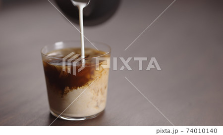 milk pour into tumbler glass with coffee on walnut table 74010140
