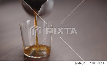 coffee pour into tumbler glass on walnut table 74010141