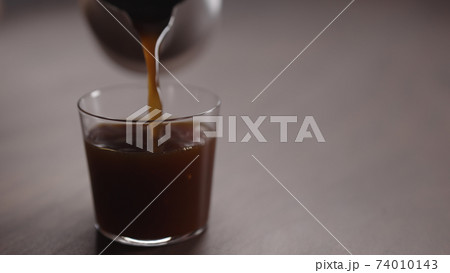coffee pour into tumbler glass on walnut table 74010143