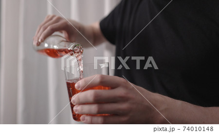 man pouring red drink into tumbler glass near window 74010148