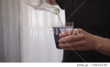 man pouring purple drink into tumbler glass near window 74010149