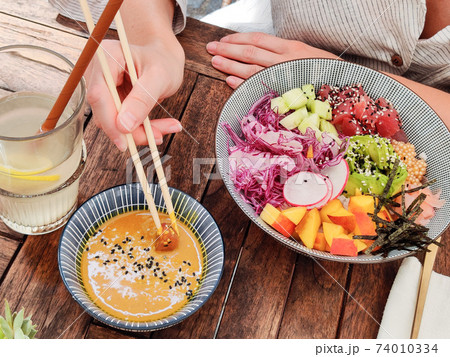 Woman eating tasty colorful healthy natural organic vegetarian Hawaiian poke bowl using asian chopsticks on rustic wooden table. Healthy natural organic eating concept 74010334