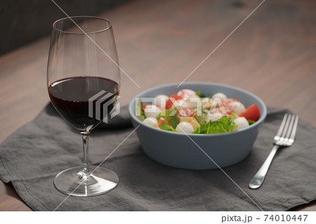 Glass of red wine with salad with romaine, tomatoes and mozzarella in blue bowl 74010447