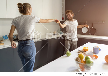 Waltzing in a new home young couple dancing celebrating their new purchase of buying their own house. Happy new family at kitchen wearing casual clothes. Love, family, happiness concept Waltzing in a new home young couple dancing celebrating their new purchase of buying their own house. Happy new family at kitchen wearing casual clothes. Love, family, happiness concept 74010732