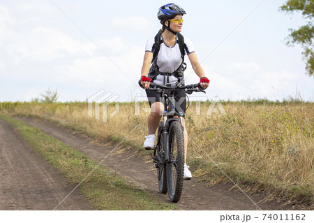 beautiful and happy woman cyclist rides a bicycle on the road in nature. beautiful and happy woman cyclist rides a bicycle on the road in nature. 74011162