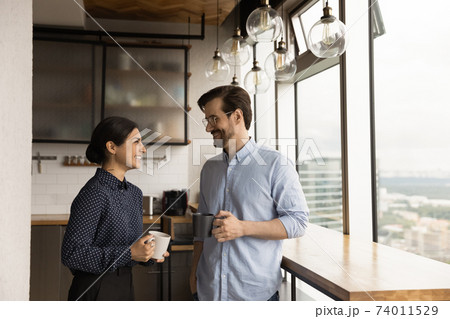 Happy mixed race couple drink tea coffee by picture window 74011529