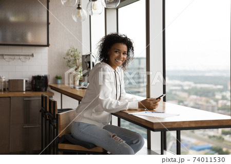 Young stylish black lady sit by table indoors hold cellphone Young stylish black lady sit by table indoors hold cellphone 74011530