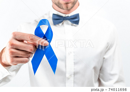 Cancer people. Hipster men in bright shirt, cyan bowtie with blue ribbon in hands on white background. Awareness prostate cancer of men health. Man Healthcare and World cancer day concept. Cancer people. Hipster men in bright shirt, cyan bowtie with blue ribbon in hands on white background. Awareness prostate cancer of men health. Man Healthcare and World cancer day concept. 74011698