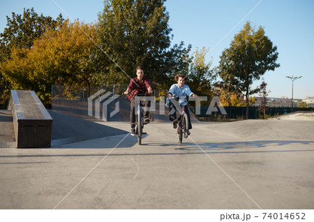 Young bmx bikers doing tricks in skatepark 74014652