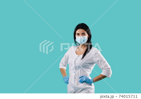 Portait on a blue background with a copy space of a young female doctor wearing medical uniform, protective mask and latex blue gloves. Healthcare concept Portait on a blue background with a copy space of a young female doctor wearing medical uniform, protective mask and latex blue gloves. Healthcare concept 74015711
