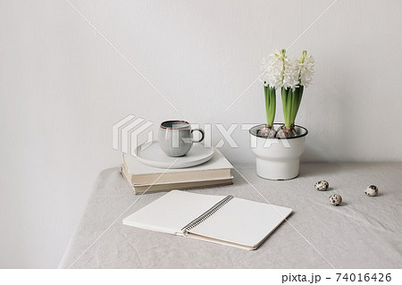 Easter spring still life. Cup of coffee, books and open diary mockup on linen table cloth. White hyacinth in flower pot. olive branches with quail eggs. Home office concept. Scandinavian interior. 74016426