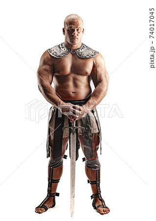 Severe barbarian in leather costume with sword. Portrait of balded muscular gladiator. Studio shot. Isolated on white background Severe barbarian in leather costume with sword. Portrait of balded muscular gladiator. Studio shot. Isolated on white background 74017045