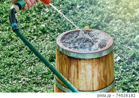 Man cleans or fills vintage oak wood tub with clear water Man cleans or fills vintage oak wood tub with clear water 74026182