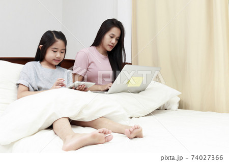 Asian mother and daugther looking laptop and tablet on bed in bedroom. Business women woking with laptop at home with her daugther smiling enjoy with tablet on bed. Work at home concept. Asian mother and daugther looking laptop and tablet on bed in bedroom. Business women woking with laptop at home with her daugther smiling enjoy with tablet on bed. Work at home concept. 74027366