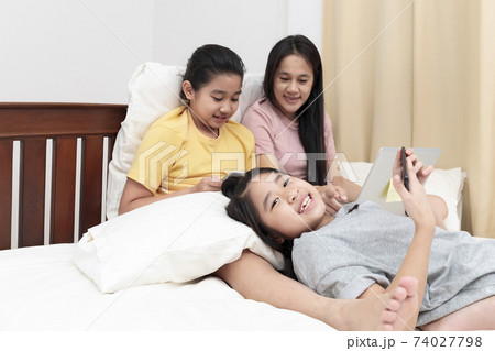 Asian family enjoy and relax on bed in bedroom. mother and daughters enjoy using laptop, tablet and smart phone together on bed.  Family concept. 74027798