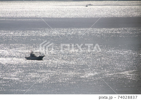 日差しを浴びてキラキラ輝く海と航行する漁船の写真素材