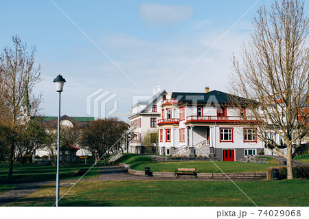 Beautiful white two-story house with a black roof, near the park in Reykjavik, the capital of Iceland. Spring town. 74029068