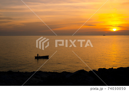 A fisherman on a boat near the shore against the backdrop of a golden sunset. 74030050