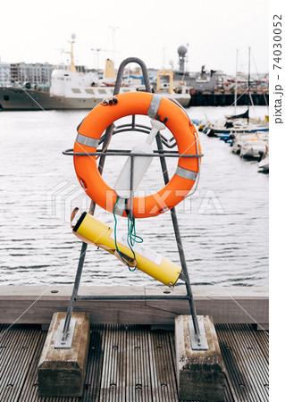 An orange lifebuoy on a stand and a kit for rescuing a drowning person and providing medical assistance in Iceland, on the pier in the port. 74030052