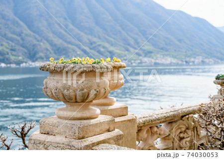 An architectural flowerpot on a stone fence against the backdrop of water and mountains. 74030053