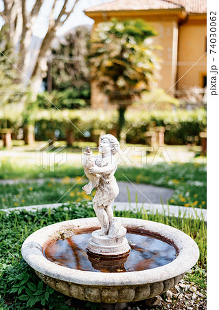 A small garden fountain in the form of a figurine of a child with a fish in his hands in the yard. 74030062