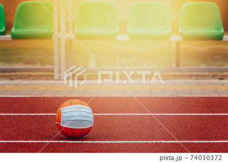 Ball with medical mask on the running track with empty stadium chairs on background Ball with medical mask on the running track with empty stadium chairs on background 74030372