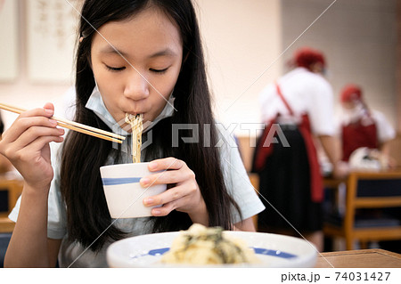 Asian teenage girl wearing face mask under the chin,woman eating food,ramen noodles in japanese restaurant at shopping mall during its reopening,new outbreak of COVID-19,safe distance,new normal life Asian teenage girl wearing face mask under the chin,woman eating food,ramen noodles in japanese restaurant at shopping mall during its reopening,new outbreak of COVID-19,safe distance,new normal life 74031427