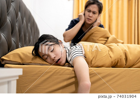 Asian daughter snoring loudly,open mouth,drooling on pillow,comfortably sleeping,annoying snoring of child girl,danger of sleep apnea disease,stressed woman or mother wakes up,closing ears with hands 74031904