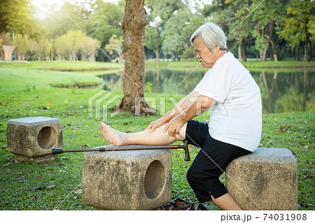 Unhappy asian senior woman with walking stick suffering from  arthritis,osteoarthritis,elderly people using hands to massage the legs,feel pain in the knee,leg injury after walking exercise in nature 74031908