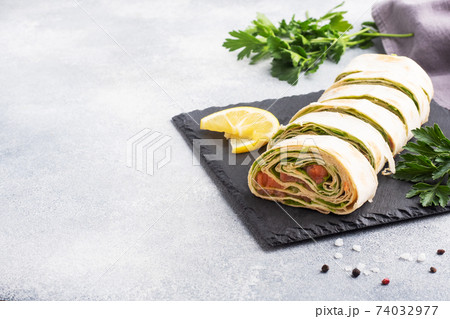 Rolls of thin pita bread and red salted salmon with lettuce leaves On a slate stand, grey concrete background. Copy space. 74032977