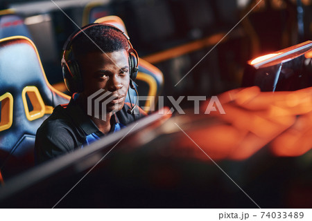 Young african guy, male professional cybersport gamer wearing headphones looking at camera while playing online video game 74033489