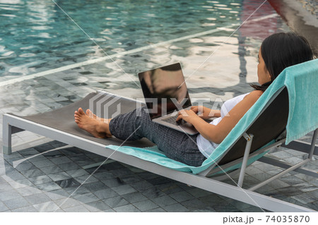 Asian freelancer using laptop while sitting at swimming pool Asian freelancer using laptop while sitting at swimming pool 74035870