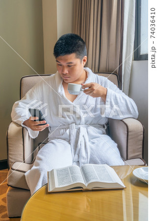 Young Asian businessman wearing bathrobe and using smartphone in hotel 74036410