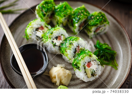 Sushi maki rolls with cucumber, avocado, tomato, creamy cheese, chuka wakame on a plate with chopsticks, soy sauce, wasabi and ginger. Japanese traditional seafood served for lunch in restaurant 74038330