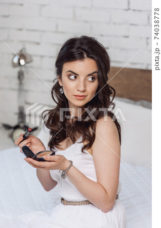 woman applying make-up while sitting on bed at the hotel room woman applying make-up while sitting on bed at the hotel room 74038778