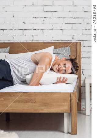 Smiling man lying on a white pillow and a mattress on a wooden bed. Concept of comfortable sleep. orthopedic mattress and pillow Smiling man lying on a white pillow and a mattress on a wooden bed. Concept of comfortable sleep. orthopedic mattress and pillow 74038793