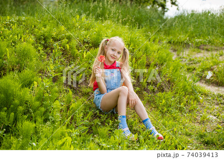 Blonde little girl with long hair and candy on a stick Blonde little girl with long hair and candy on a stick 74039413