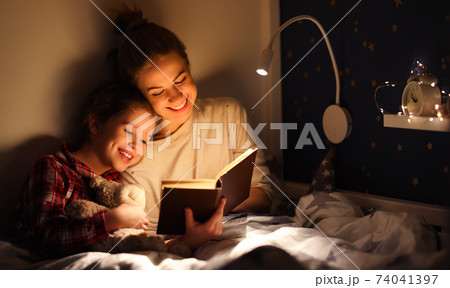 Happy mother and daughter reading book together on bed Happy mother and daughter reading book together on bed 74041397