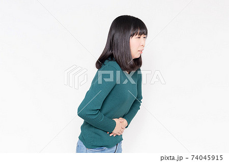 白背景の前に立って、お腹に手を当てている女性 74045915