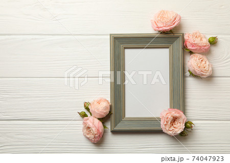 Roses and blank frame on white wooden background 74047923
