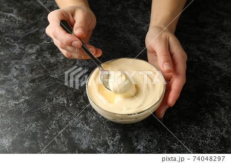 Female hands hold spoon and bowl with mayonnaise on black smokey background Female hands hold spoon and bowl with mayonnaise on black smokey background 74048297