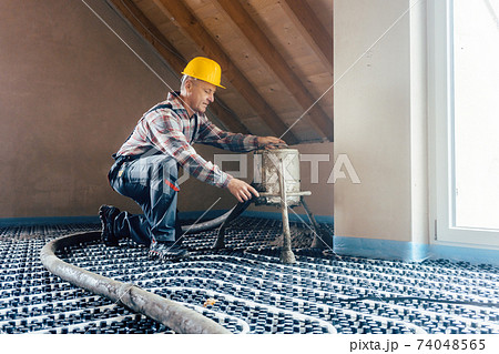 Worker on construction site installing pipes for underfloor heating 74048565