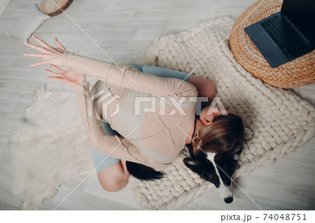 Adult mature woman doing yoga at home in living room with corgi dog pet with online tutorials on laptop Adult mature woman doing yoga at home in living room with corgi dog pet with online tutorials on laptop 74048751