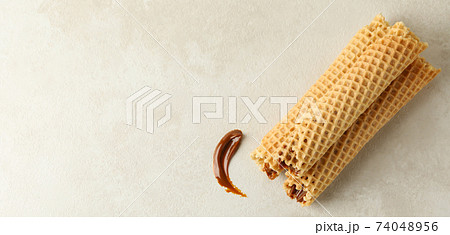 Tasty wafer rolls with condensed milk on white textured background 74048956