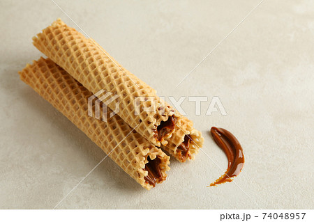 Tasty wafer rolls with condensed milk on white textured background 74048957