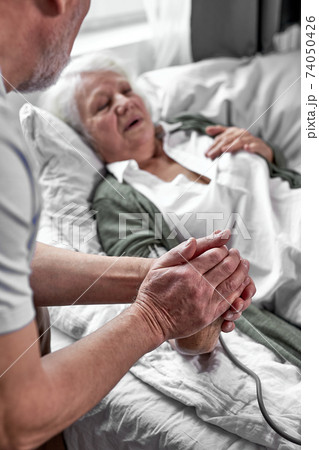 loving mature man supporting his sick wife lying on bed loving mature man supporting his sick wife lying on bed 74050426